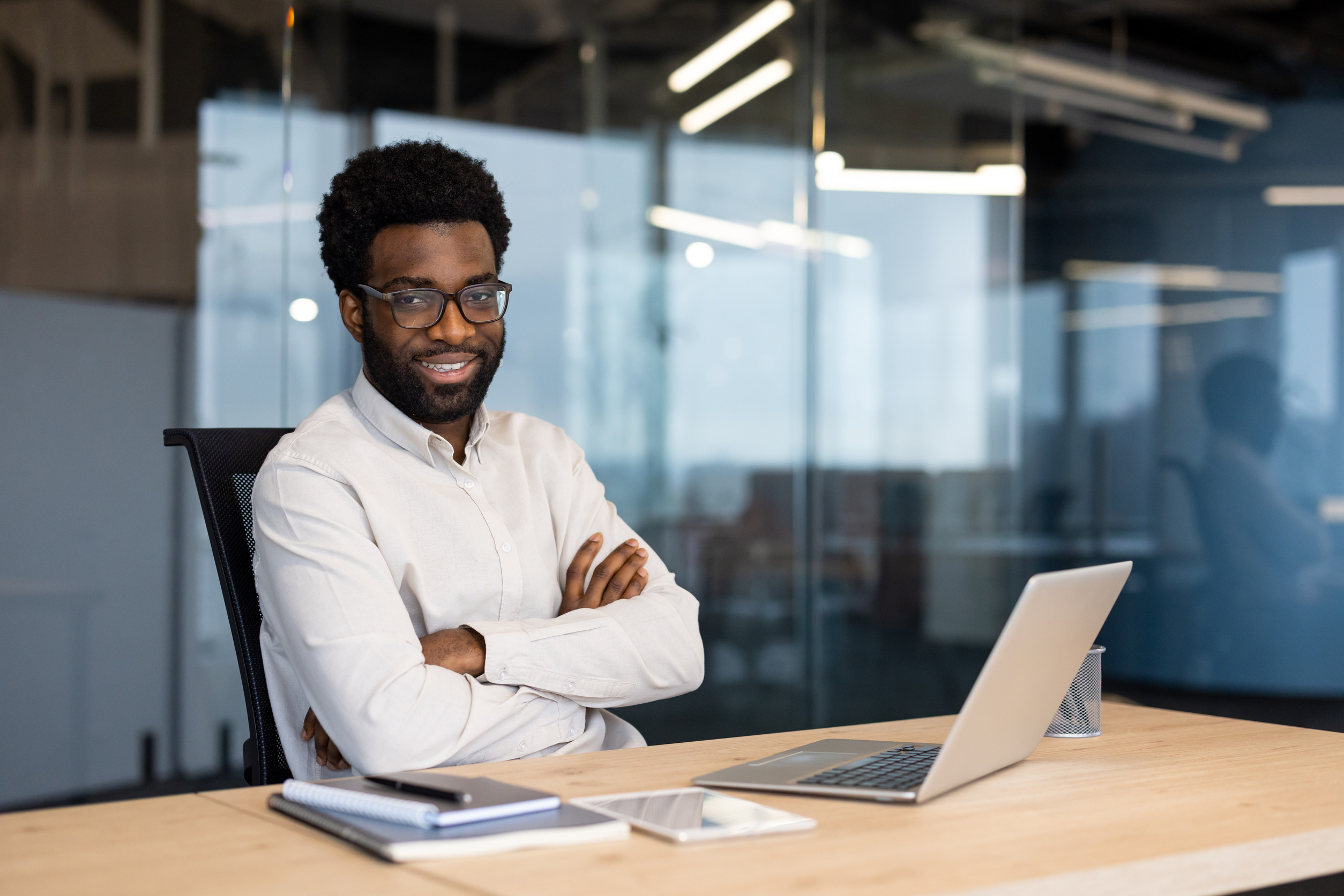 portrait of a young happy entrepreneur, businessman smiling and looking at the camera, sitting at a desk with a laptop inside a company office, man in business clothes